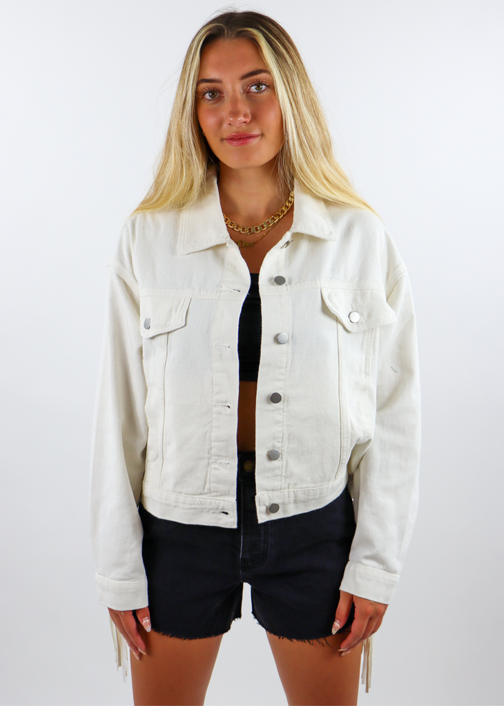 white denim jacket with silver buttons and fringe going across the entire back.